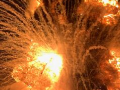 Cena caótica quando uma fábrica pega fogo, blocos de concreto e um tanque químico voam no ar