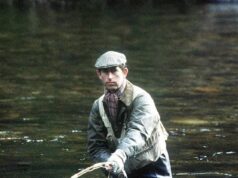 O experiente pescador Charles usa a mira telescópica de seu rifle de segurança para ajudá-lo a localizar salmões.