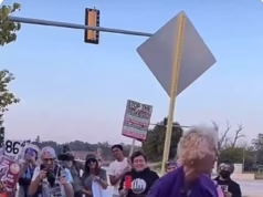 Uma mulher de cabelos grisalhos com uma camiseta ‘Make America Kind Again’ é filmada batendo alegremente em uma pinata de Donald Trump com uma barra de metal.