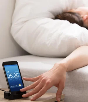 woman-reaching-snoozing-cell-phone-alarm-clock.webp