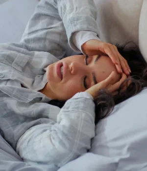 woman-stress-headache-bed-sick-hangover-sleep.webp