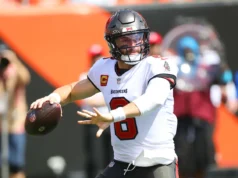 Baker Mayfield veste uma regata do Michigan para pagar uma aposta com Todd Bowles após a vitória dos Wolverines sobre Oklahoma.